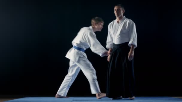 Kampfkunst-Aikido-Meister mit Hakamas bringt seinem jungen Schüler bei, wie er sich gegen einen Angriff verteidigen kann. Schuss isoliert auf schwarzem Hintergrund. — Stockvideo