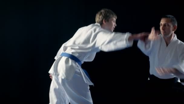 Martial Arts Aikido Master Wearing Hakamas Teaches Young Student How to Defend Himself Against an Attack. Hand Grab Technique. Shot Isolated on Black Background. — Stock Video