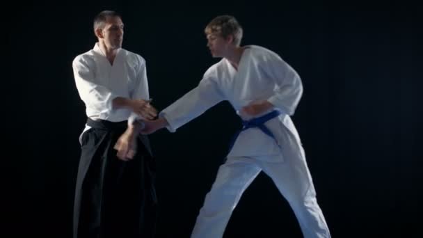 Maestro di Arti Marziali Indossa Hakamas Insegna Tecnica Giovane Studente Aikido. Girato isolato su sfondo nero e in slow motion . — Video Stock