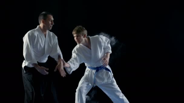 Harcművészetek mestere, Hakamas visel tanítja a fiatal diák Aikido technika dobott át a vállát. Lövés a fekete háttér, és a lassú mozgás. — Stock videók