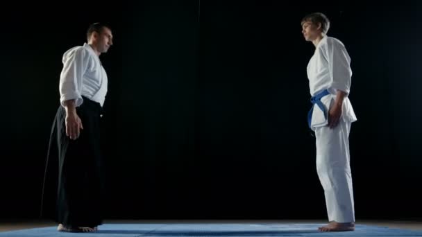 Martial Arts Master Wearing Traditional Samurai Hakamas and His Young Student Bow to Each Other and Take Battle Stance. Shot Isolated on Black Background and in Slow Motion. — Stock Video