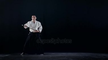 Aikido Ana giyim geleneksel samuray Hakama giysiler ile Japon kılıcı kın ve salıncaklar dışarı alır. Onu o spot karanlık çevreler. Siyah arka plan üzerine izole atış.