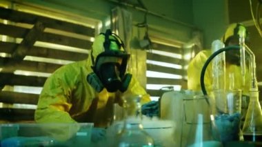 Yeraltı uyuşturucu laboratuarında koruyucu maskeler ve tulum giyen iki gizli kimyagerler pişmiş ilacın saflık ve gücü Test edin. Onlar terk edilmiş iş bina cam eşyalar dolu ve pişirme ekipmanları.