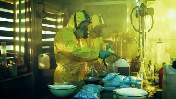 В подпольной лаборатории два тайных химика готовят наркотики. Они носят маски и комбинезоны и работают с стаканами и токсичными химическими соединениями . — стоковое видео