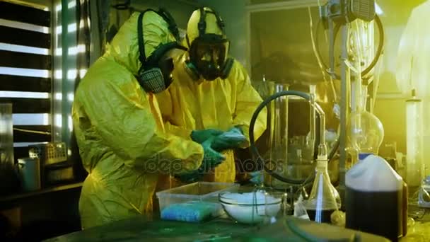 Nel laboratorio sotterraneo due chimici clandestini che indossano maschere protettive e tute confezionano borse di metanfetamina sintetica in scatole per un'ulteriore distribuzione. Il laboratorio è pieno di attrezzature illegali. Si accovacciano in un edificio abbandonato . — Video Stock