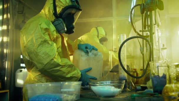 In het laboratorium van de ondergrondse Drug bedekt twee clandestiene chemici met beschermende overall en gasmaskers Mix chemicaliën om Drugs synthetiseren. Ze werken in de verlaten gebouw. — Stockvideo