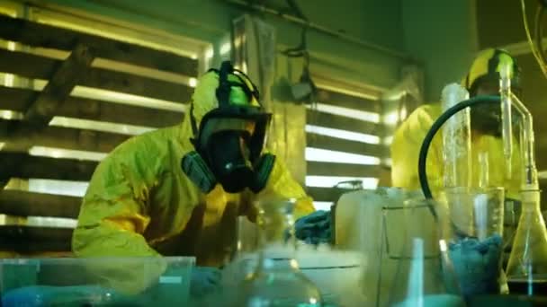 Nel laboratorio sotterraneo di droga due chimici clandestini che indossano maschere protettive e tute testano la purezza e la forza della droga cotta. Lavorano nell'Edificio Abbandonato Pieno di Vetreria e Attrezzature da Cucina . — Video Stock