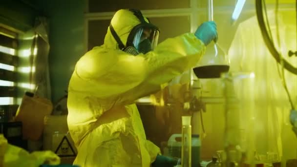 In het laboratorium van de ondergrondse Drug mengen clandestiene chemici dragen van beschermende maskers en overall chemicaliën. Men giet vloeistof uit de bus in Bowl, tweede controles bekerglas voor Product consistentie. Ze werken in de verlaten gebouw. — Stockvideo