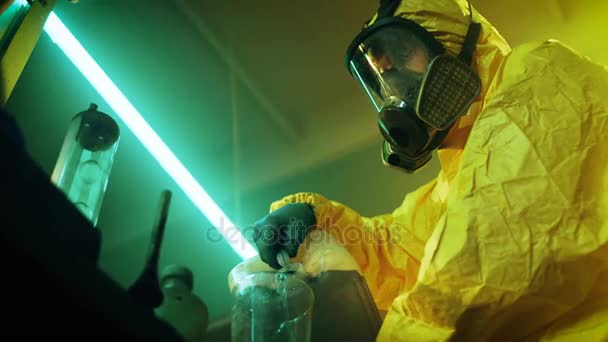 In the Underground Drug Laboratory Clandestine Chemist Wearing Protective Mask and Coverall Mixes Chemicals. Il verse du liquide de la boîte dans le bol pour fabriquer un nouveau lot de stupéfiants synthétiques. Il squats dans le bâtiment abandonné . — Video
