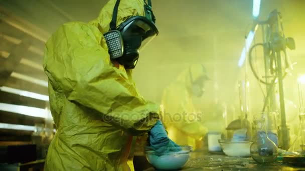 I underjordiska drog laboratorium två hemliga kemister koka krossa syntetiska droger, dem i en skål och paketet för vidare Distribution. De bära skyddande Gas masker och överdragskläder och knäböj i övergivna byggnaden. — Stockvideo