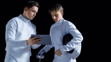 İki genç tam donanımlı eskrimcilerin strateji, saldırı ve savunma eskrim hakkında daha fazla bilgi için Tablet bilgisayar kullanın. Siyah arka plan üzerine izole atış.