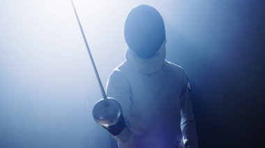 Tam donanımlı Fencer koyar asansörleri folyo kılıç bir maç için hazır. Karanlık etrafında onu ise sahne ışıkları altında duruyor. Siyah arka plan üzerine izole atış.