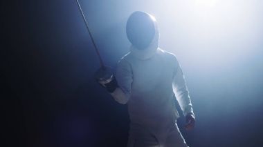 Tam donanımlı Fencer koyar asansörleri folyo kılıç bir maç için hazır. Karanlık etrafında onu ise sahne ışıkları altında duruyor. Siyah arka plan üzerine izole atış.