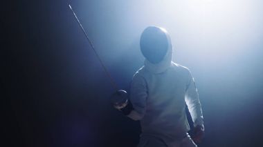 Tam donanımlı Fencer koyar asansörleri folyo kılıç bir maç için hazır. Karanlık etrafında onu ise sahne ışıkları altında duruyor. Siyah arka plan üzerine izole atış.