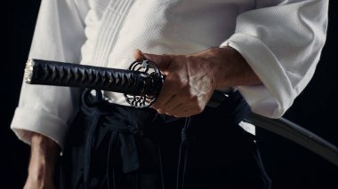 Aikido ustası geleneksel samuray Hakama elbise giyen Japon kılıcı kın içinde tutar. Onu o spot karanlık çevreler. Siyah arka plan üzerine izole atış.