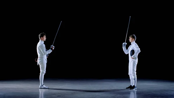두 젊은 전문 Fencers 인사 서로, 그리고 일치를 싸움에 대 한 준비. 총 검은 배경에 고립. — 스톡 사진