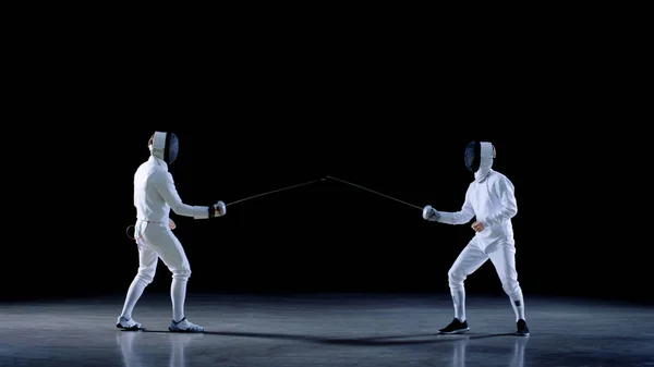 두 젊은 전문 Fencers 인사 관객, 마스크와 일치 싸우는 시작 칼에. 총 검은 배경에 고립 . — 스톡 사진