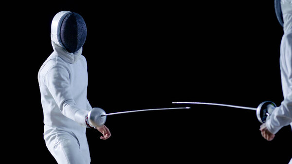 Two Professional Fencers Show Masterful Swordsmanship in their Foil Fight. They Attack, Defend, Leap and Thrust and Lunge. Shot Isolated on Black Background.