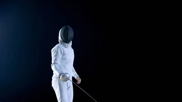 Treinamento de esgrimista qualificado totalmente equipado com uma folha metálica. Ele pratica ataque, defesa, salto, impulso e Lunge. Tiro isolado no fundo preto . — Fotografia de Stock