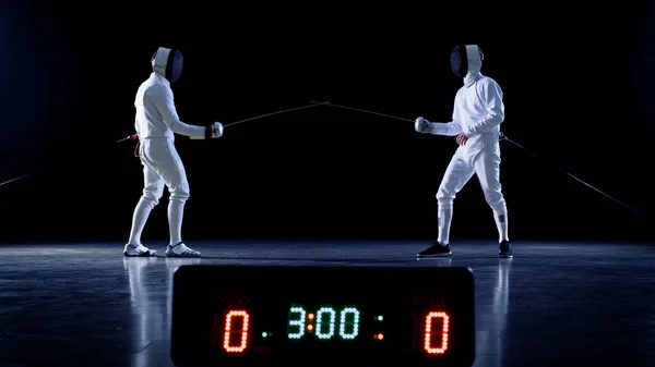 На Чемпионате Два Профессиональные полностью оборудованные фехтовальщики готовы к бою с фольгой, в то время как табло держит очки хитов. Съемки на изолированном чёрном фоне . — стоковое фото