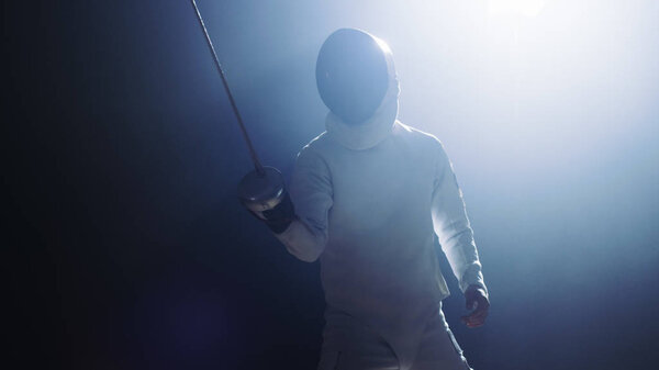 Полностью экипированный "Фенкер" поднимает меч из фольги в готовности к матчу. Он стоит в центре внимания, в то время как тьма вокруг Него. Выстрел на черном фоне
.