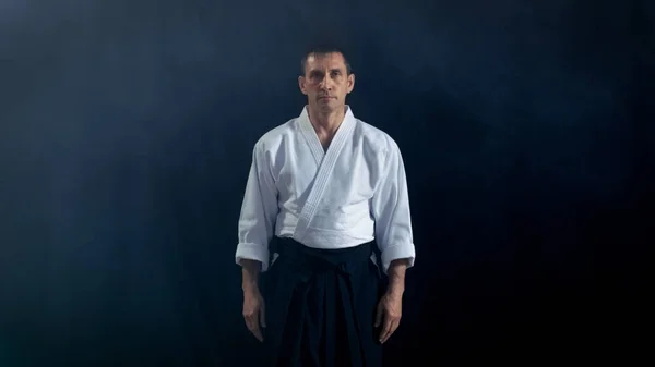 Retrato Tiro do Mestre Aikido Vestindo Roupas Samurai Hakama Tradicionais Olhando para a câmera. Ele está no Spotlight Darkness rodeia-o. Tiro isolado no fundo preto . — Fotografia de Stock