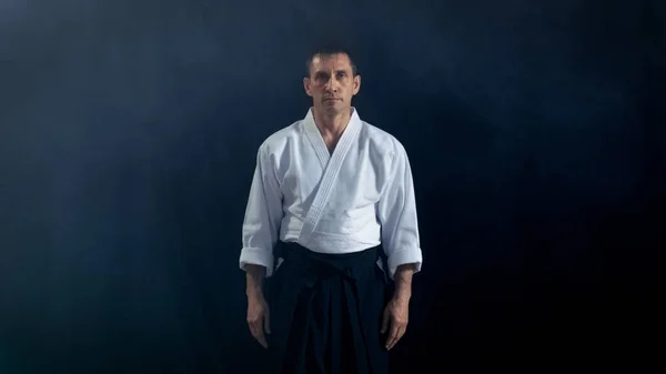 초상화 샷 합기도 마스터의 카메라를 살펴보고 전통적인 사무라이 Hakama 옷을 입고. 그 스포트 라이트 어둠 주변에 그 는입니다. 총 검은 배경에 고립. — 스톡 사진