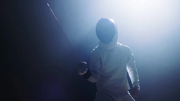 Fully Equipped Fencer Puts Lifts Foil Sword in Readiness for a Match. He Stands in the Spotlight while Darkness is Around Him. Shot Isolated on Black Background. — Stock Photo, Image