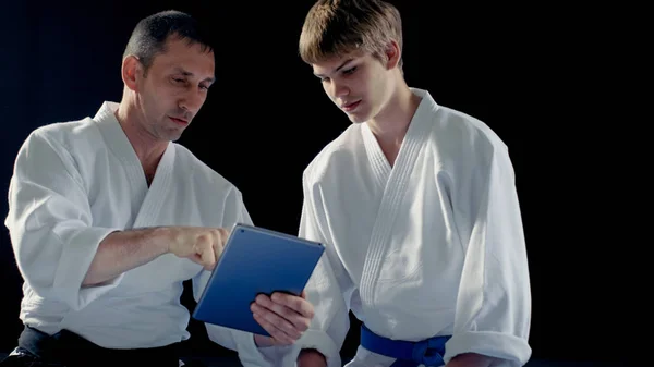 Maestro de artes marciales con Hakamas enseña técnica de Aikido joven estudiante con la ayuda de la Tablet Computer. Disparo aislado sobre fondo negro . — Foto de Stock