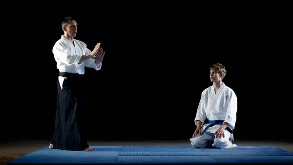Майстер бойових мистецтв показує красиві методи боротьби Айкідо зі своїм учнем, який дивиться на нього з найбільшою повагою. ізольовано на чорному тлі . — стокове фото