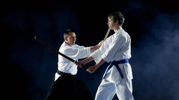 Kampsportsmästare lär hans ung Student hur man slåss med Wooden Sword Bokken. Sparring slutar i sekunder, Master Wins. Skott är isolerad på svart bakgrund. — Stockfoto