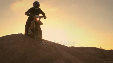 Profesyonel motokros motosiklet binici sürücülerde Dune ve üst üzerinde durur. Günbatımı zamanı ve parça dumanla kaplı / sis.