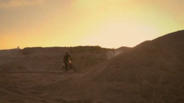 Profesyonel motokros motosiklet binici sürücüler kumul üzerinde ve daha fazla Off-Road parça aşağı. O gün batımı ve parça dumanla kaplı / sis.