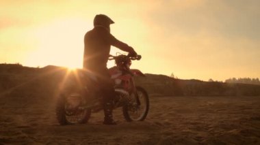 Fmx motosiklet binici Onun Bisiklet ve bakan zor Sandy Off-Road arazi üzerinde duruyor. Güneş batıyor.