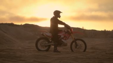 Fmx motosiklet binici Onun Bisiklet ve bakan zor Sandy Off-Road arazi üzerinde duruyor. Güneş batıyor.