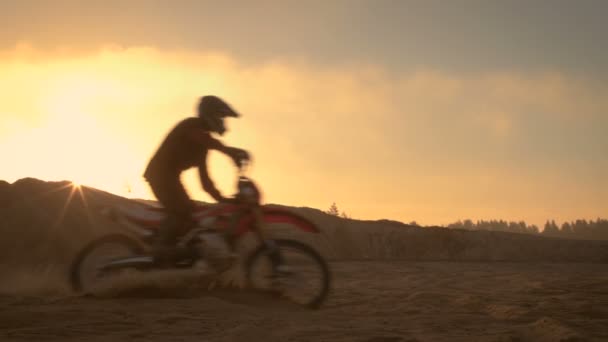 プロのモトクロス ライダーは、オフロードの砂の地形のドライブします。それは日没とトラックは、煙や霧、もやのかかった日光で覆われています。. — ストック動画
