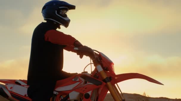 Professionele Fmx motorrijder bereidt om te beginnen met het rijden op zijn fiets Over harde zandige Off-Road terrein. Zon ondergaat. — Stockvideo