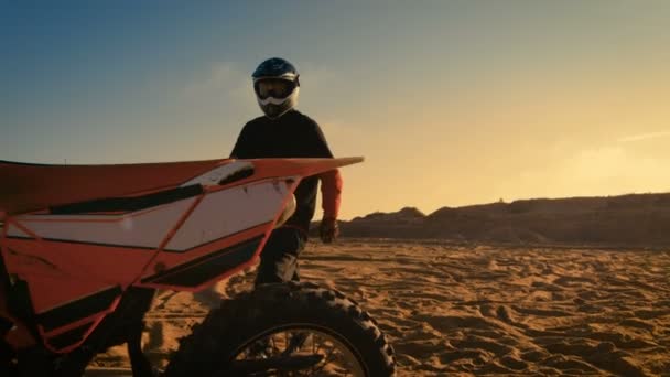Frontaufnahme des professionellen Motocross-Fahrers, wie er sein fmx-Dirt-Bike auf der Sand / Dirt-Track-Strecke sattelt. — Stockvideo