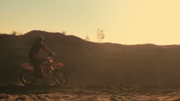 Vista lateral Shot Motocross profesional motociclista conduce en la duna y se detiene. Es puesta del sol y la pista está cubierta con humo / niebla . — Vídeo de stock