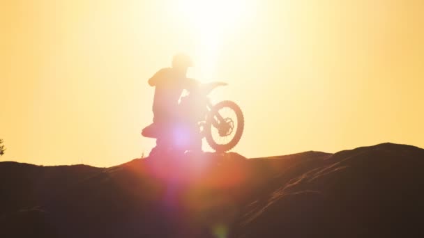 Professionelle Motocross-Fahrer auf fmx Motorrad macht Wheelie auf der Düne und fährt davon. Seine Silhouette ist mit untergehender Sonne auf dem Hintergrund zu sehen. — Stockvideo