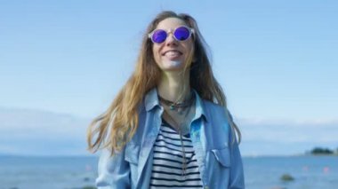 Güzel genç genç kız kahverengi saçlı serin güneş gözlüğü takmış Holi renkli toz hava ve gülüyor atar. Onu ve onun arkasında Deep Blue Sea arkasında açık mavi gökyüzü.