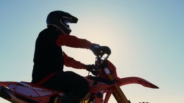 Video a basso angolo del pilota professionista di motocross su stand di moto FMX nel mezzo della cava e si affaccia su terreni estremi fuoristrada che cavalcherà oggi . — Video Stock