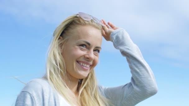 Beautiful Young Woman with Long Blonde Hair and Aviator Glasses Smiles on Camera with Clear Blue Sky on the Background. — Stock Video