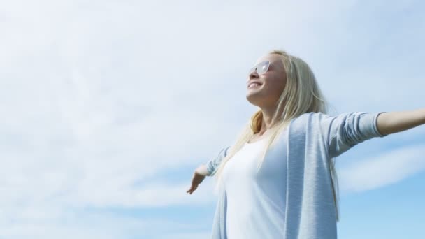 Mooie jonge vrouw met lang blond haar met de armen wijd Open om te vieren van haar succes en Warm weer. Sun is Shining en de lucht is blauw. — Stockvideo