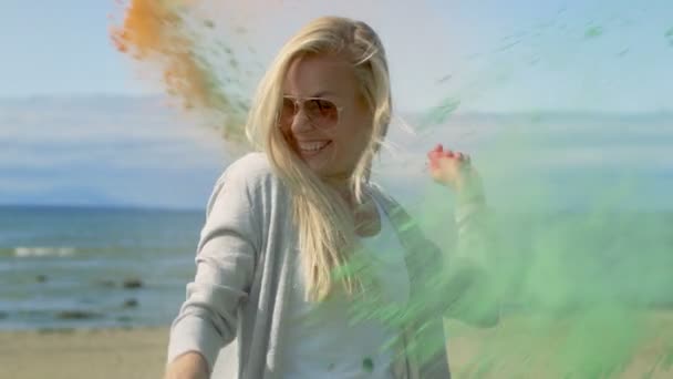 Beautiful Young Young Girl with Blonde Hair Wearing Cool Sunglasses is Hit by a Colorful Holi Powder, Throws Some in Return and Laughs. Clear Blue Sky Behind Her and Deep Blue Sea Behind Her. — Stock Video
