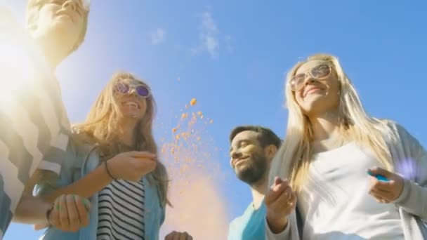 Low-Winkelaufnahme einer multiethnischen Gruppe unterschiedlicher junger Leute, die tanzen und buntes Pulver in die Luft werfen, um das Holi-Fest zu feiern. Sie haben enormen Spaß an diesem sonnigen Tag. — Stockvideo