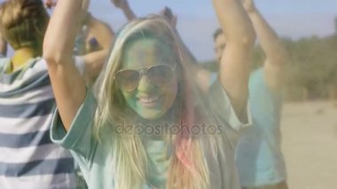 Güzel sarışın kız dansları kutlama Holi Festivali'nin arkadaşları ile yakın çekim portre. Onu yüz ve kıyafet renkli toz ile kaplıdır. İnsanlar arka planda dans.