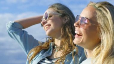 İki güzel mutlu kız güneş gözlüğü takıyor portre çekim kucaklamak, gülmek ve çok eğlenecek. Açık mavi gökyüzü arka planda görülür. 