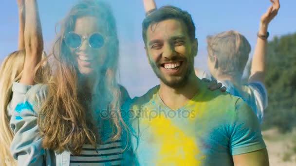 Boldog pár szereplő színes por tánc a Holi fesztivál. Akik a háttérben szórakoztató dobja Holi por. — Stock videók