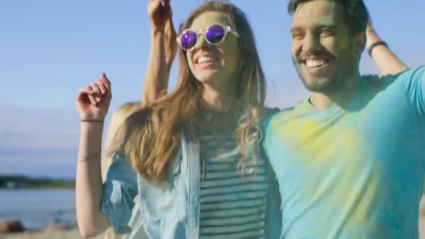 Retrato de una feliz pareja cubierta de colorido polvo bailando en el festival Holi. La gente en el fondo se divierten tirar Holi polvo . — Vídeos de Stock